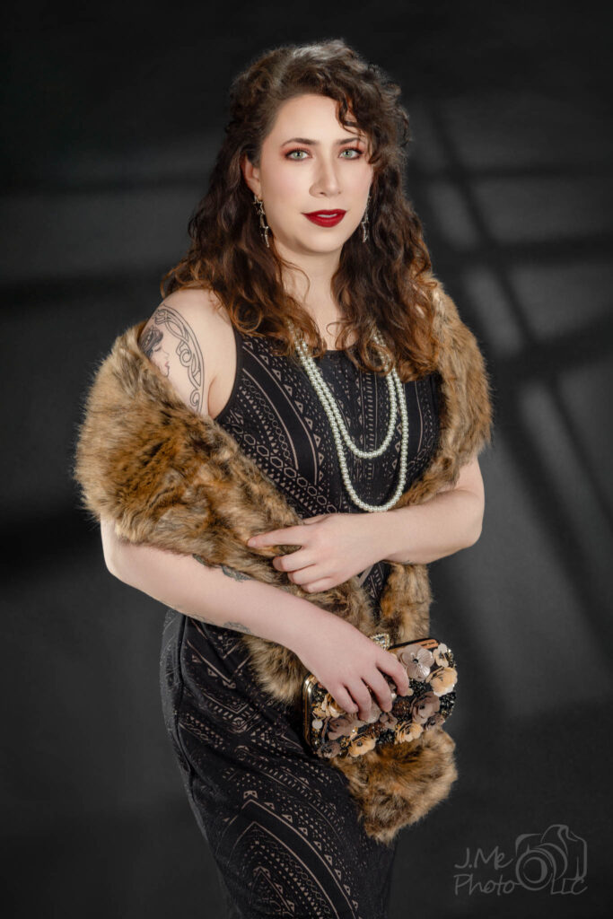 Alysia in a black beaded dress and tan fur stole with long pearls, a hard window shadow on the wall behind her