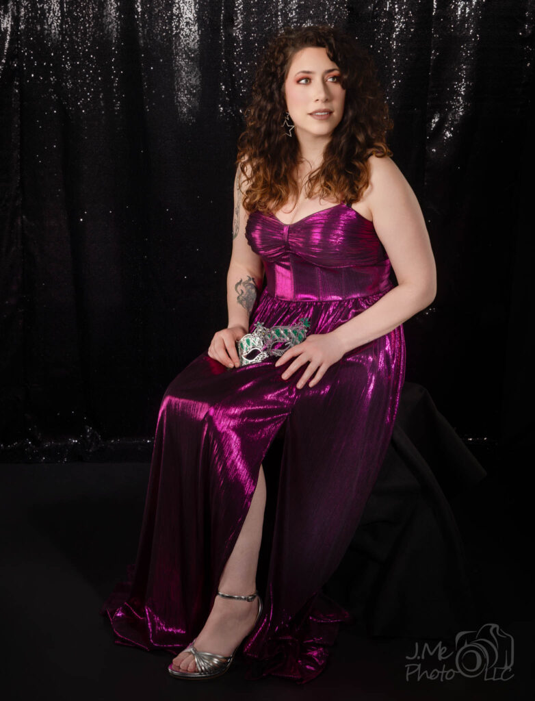 Alysia in a magenta metallic gown, seated against a silver tinsel curtain