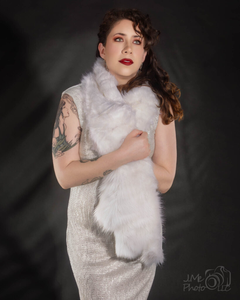 Alysia in the cream beaded dress with a white fur stole, against the same shadowed wall