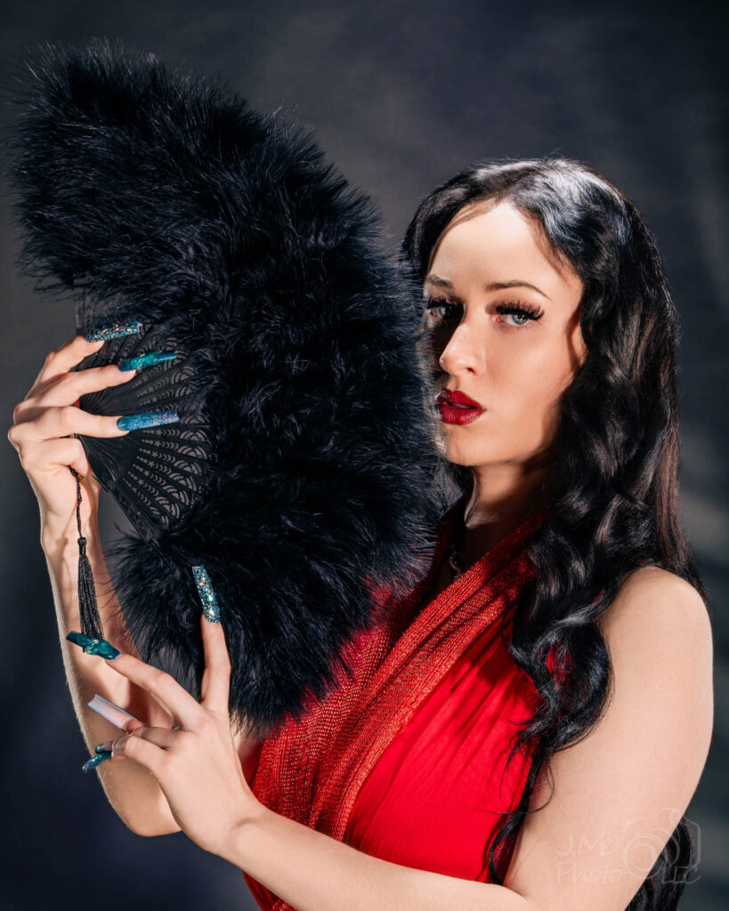 Autumn in a red dress holding a large black feather fan against a softly mottled ground