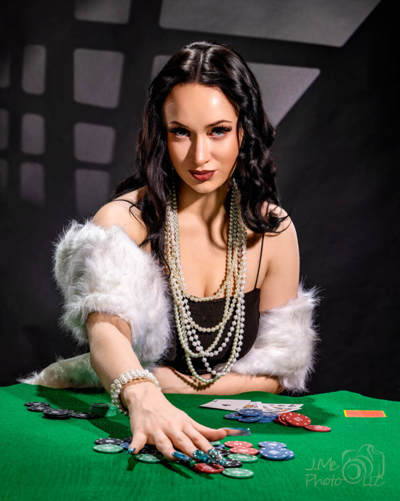 Autumn in a black beaded dress and white fur at a green card table, chips and cards in front of her, a window shape thrown on the wall behind