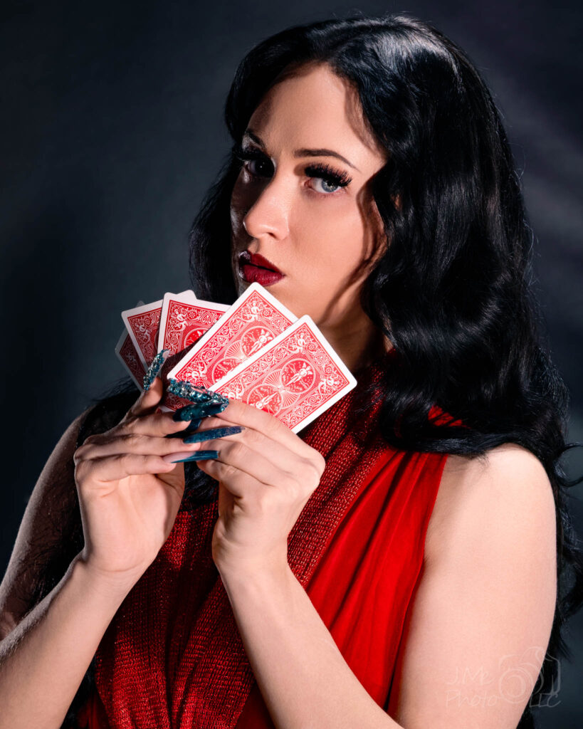 Close portrait of Autumn in a red dress holding three playing cards in front of her face